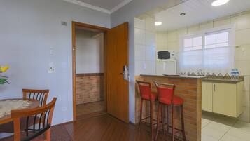 Una cocina compacta con una mesa de comedor de madera y sillas, una pequeña barra con taburetes, y un microondas visible.