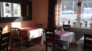 A restaurant with tables set for dining, chairs, and a window view. - Hotel Restaurant Achilles (Kirkel)