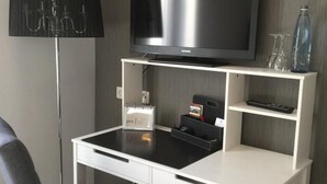 A compact hotel room with a flat-screen TV mounted on a white desk, a small refrigerator, a chair, and a lamp. - Hotel Restaurant Achilles (Kirkel)