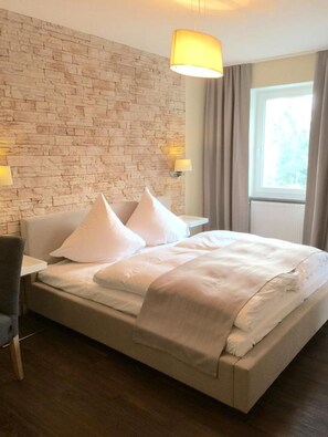 A hotel room with a brick-patterned wall, a bed with white bedding, two bedside lamps, and a window with curtains. - Hotel Restaurant Achilles (Kirkel)