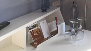 A hotel room with a white console table, a remote control, a magazine rack with a book, and three wine glasses. - Hotel Restaurant Achilles (Kirkel)