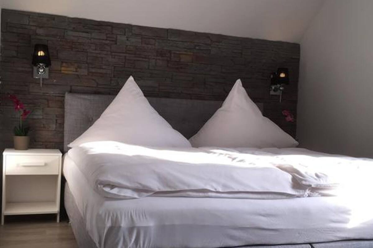 A bedroom with a bed, two nightstands, a stone wall, and a potted plant.