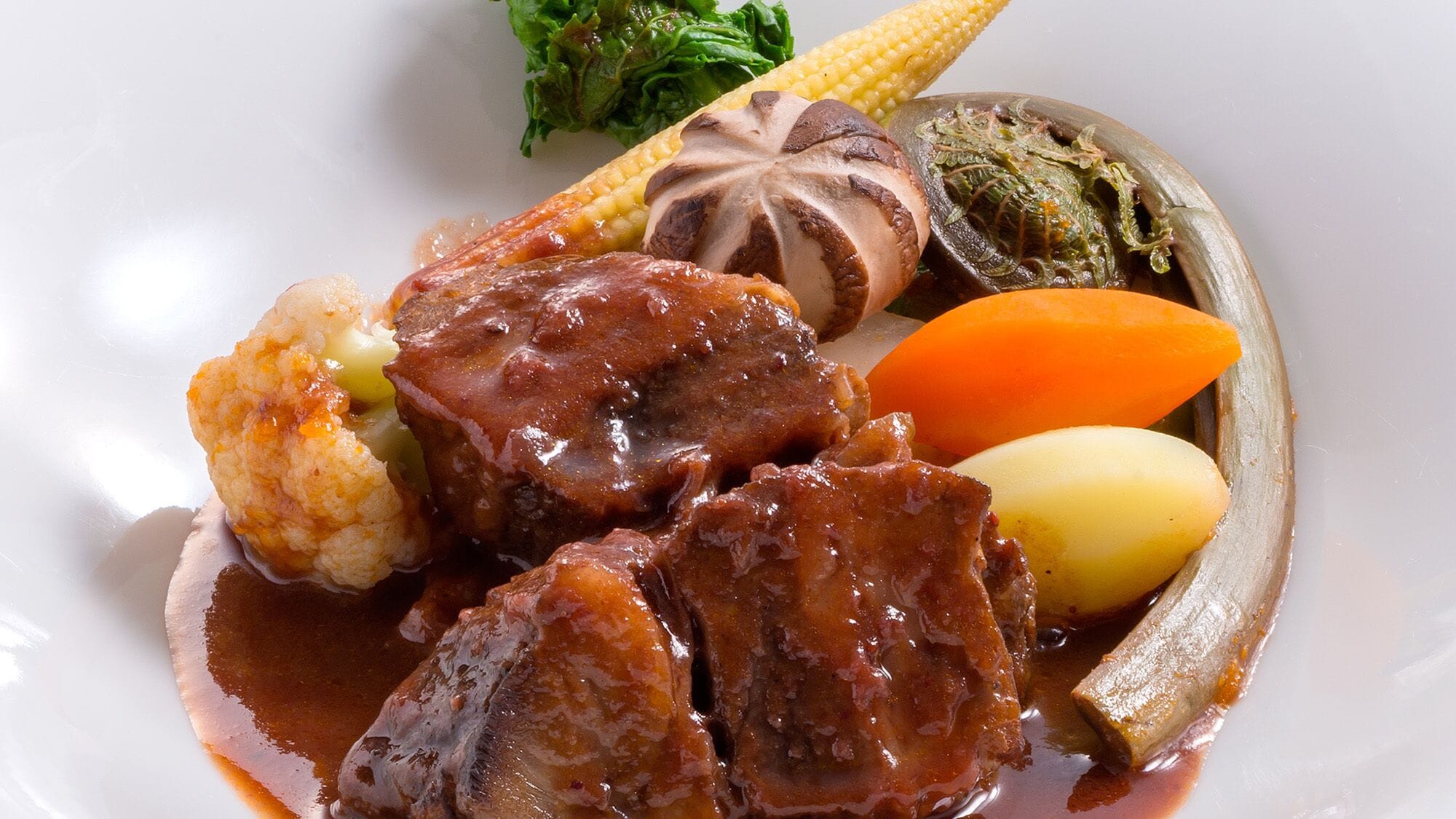 A plate with a variety of food items including meat, vegetables, and a corn cob.