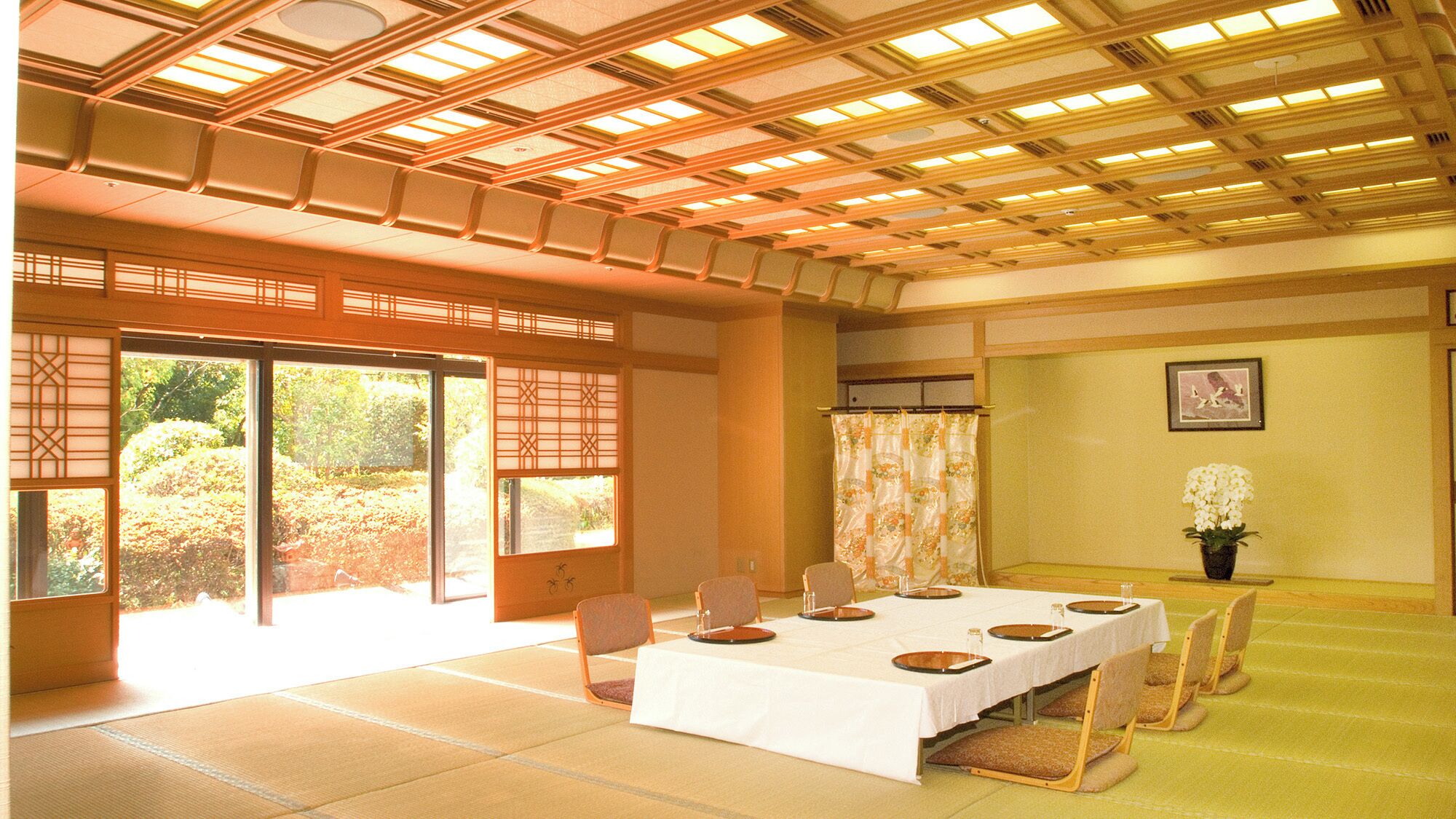 Ein traditioneller japanischer Raum mit Tatami-Böden, einem niedrigen Esstisch und Schiebetüren zu einem Garten.