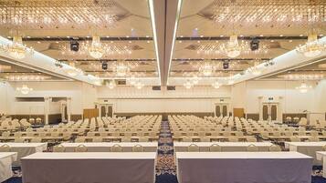 A large conference room with rows of tables and chairs, ornate chandeliers, and a carpeted floor.