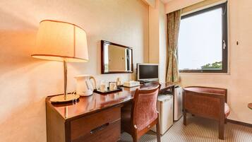 A hotel room with a desk, a chair, a lamp, a television, and a window with a view.