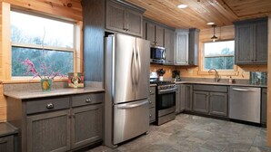 A modern kitchen with grey cabinets, stainless steel appliances, and a large window providing natural light.