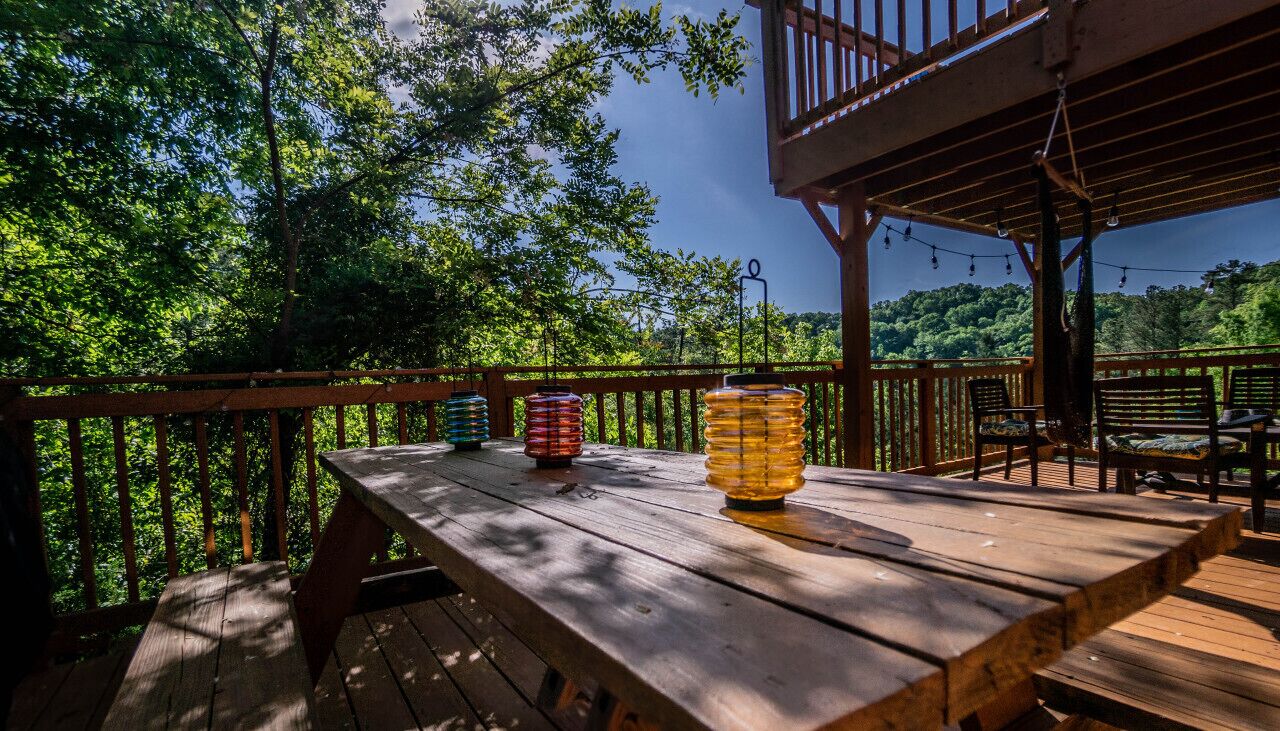 Um deck de madeira com mesa e cadeiras, ladeado por um corrimão de madeira, com vista para uma área arborizada.