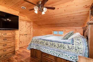 A wooden cabin bedroom with a bed, dresser, and ceiling fan.