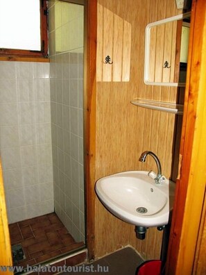 A small bathroom with a wooden door, a white sink, and a shower area.