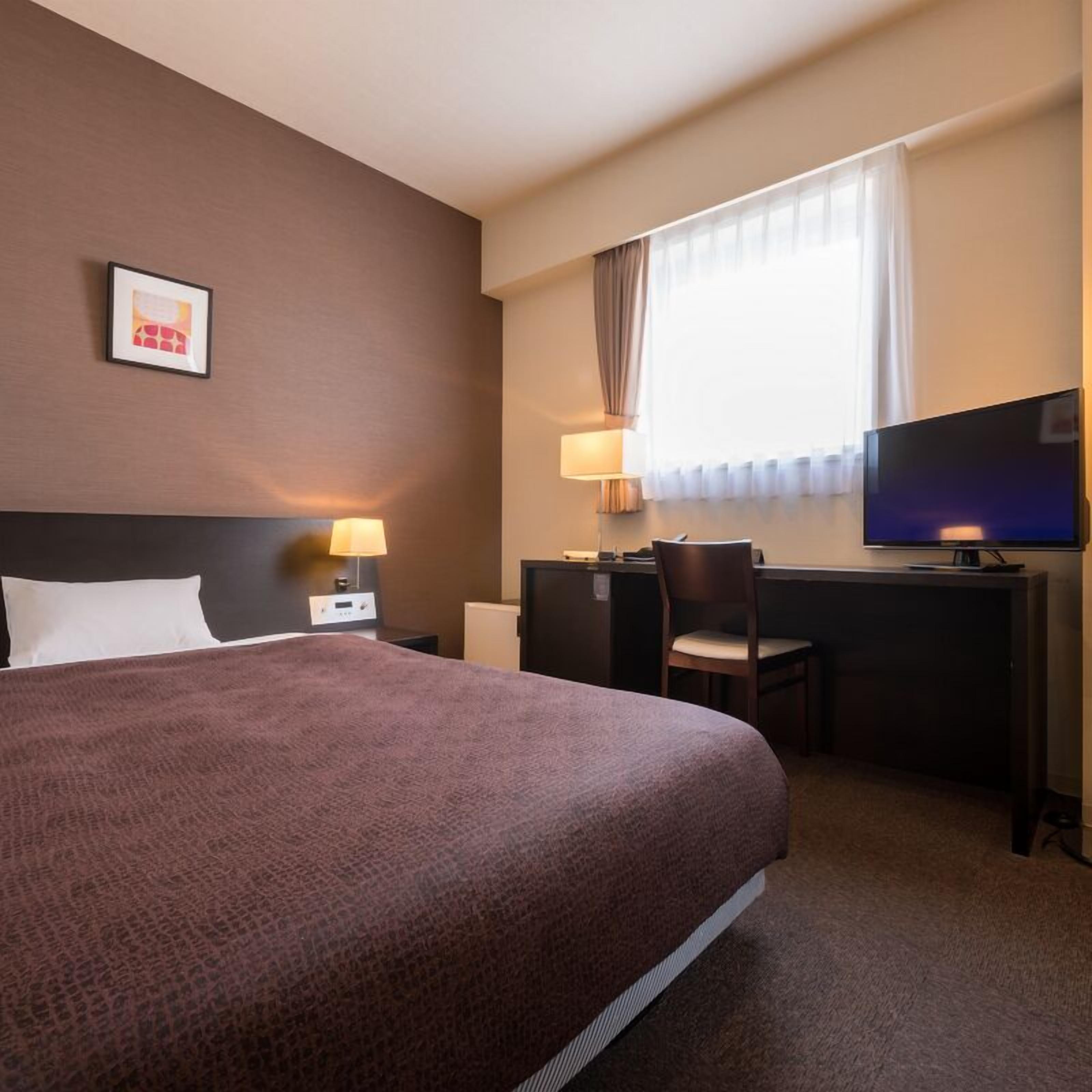Une chambre d’hôtel équipée d’un lit, d’un bureau, d’une chaise, d’une télévision et d’une fenêtre avec des rideaux.