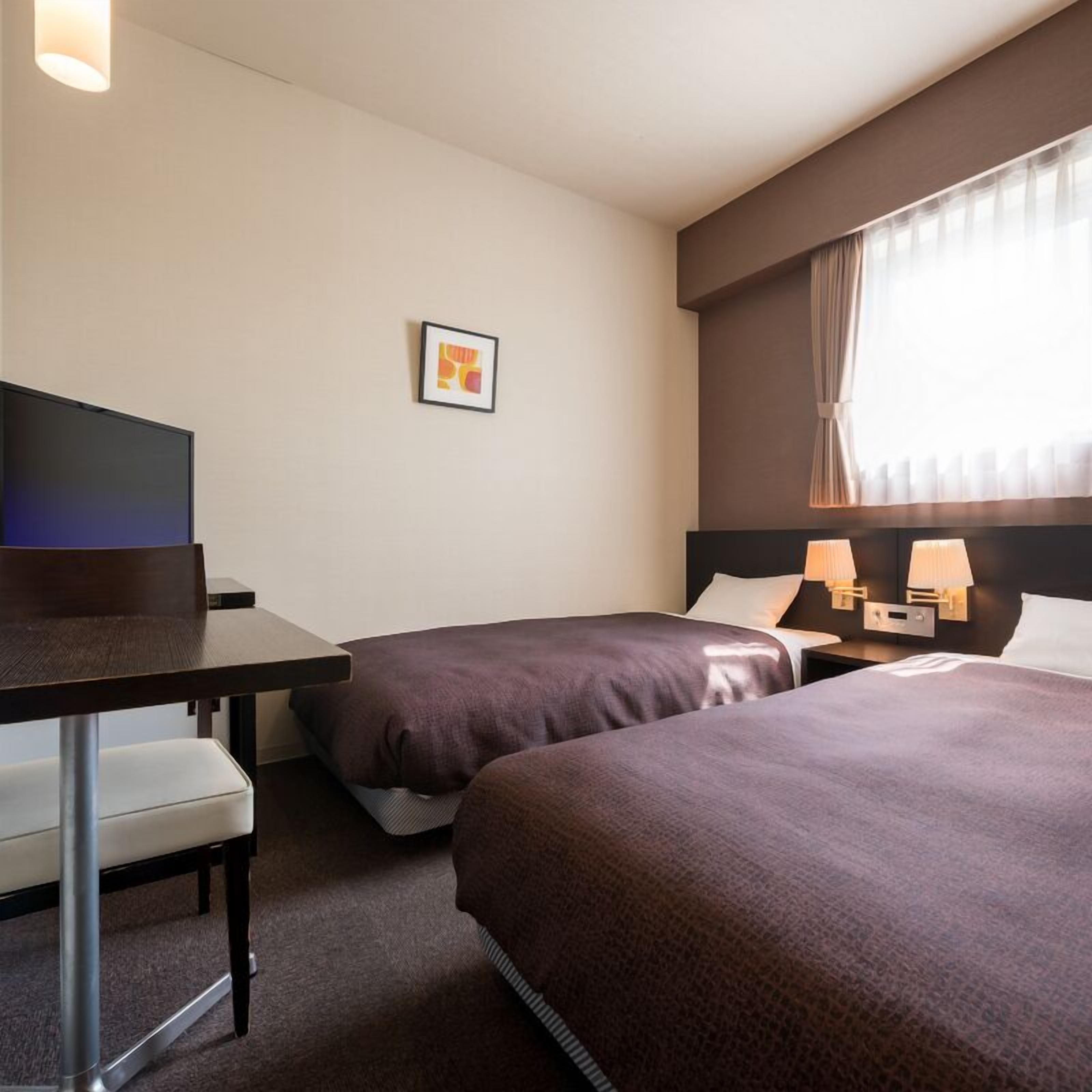 Una habitació d'hotel amb dos llits, un escriptori, una cadira, un televisor i un quadre amb marc a la paret.