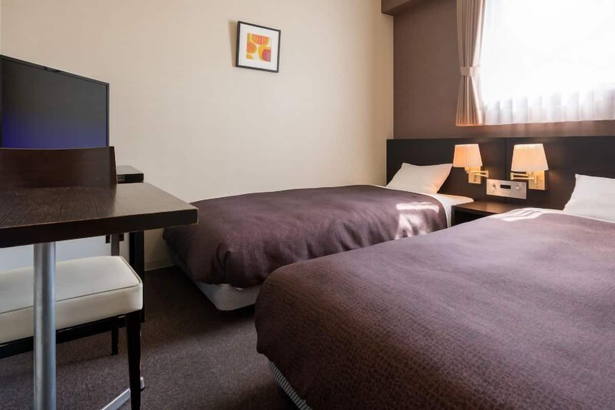 Una habitació d'hotel amb dos llits, un escriptori, una cadira, un televisor i un quadre amb marc a la paret.