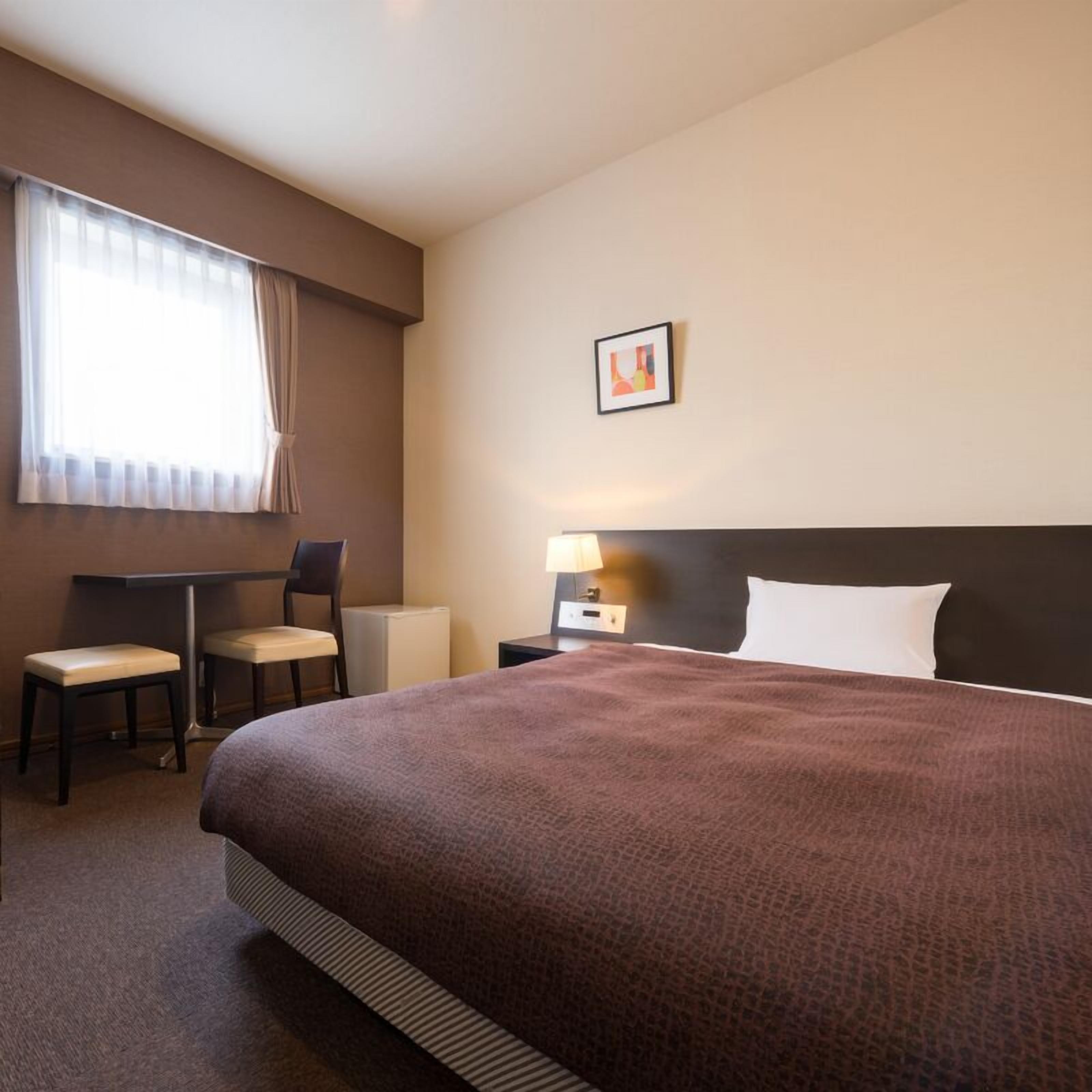 Une chambre d’hôtel avec un grand lit, un bureau avec deux chaises, une table de chevet avec une lampe et un tableau encadré au mur.