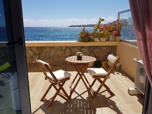 A balcony with a stone wall, two wooden chairs, a small round table, and potted plants. - Large bright studio with terrace on the beach with sea and city view (Ajaccio)