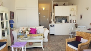 En kompakt opholdsstue med sofa, to stole, et lille bord og et tekøkken.