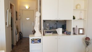 Et lille køkken med hvide skabe, en vask og en bordplade. En statue står på bordpladen, og der er forskellige køkkenartikler synlige.