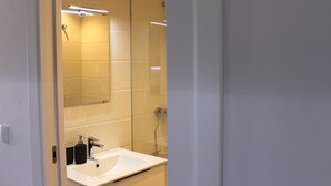 Ein modernes Badezimmer mit einem weißen Waschbecken, einem Spiegel und einer Duschkabine aus Glas.