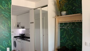 Eine moderne Küche mit Waschmaschine, Mikrowelle und Kühlschrank. Eine Schiebetür führt in einen weiteren Raum.