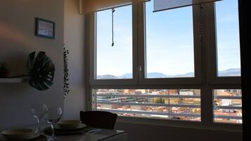 Un comedor con una mesa dispuesta para dos, vista a la ciudad a través de amplias ventanas y una planta en la pared.