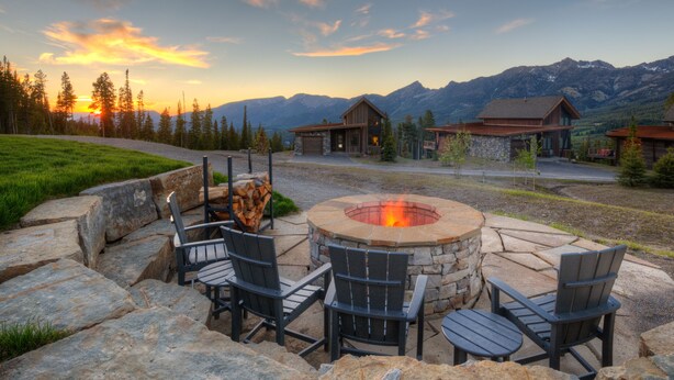 A stone fire pit with chairs, surrounded by a stone patio, with a mountain view in the background. - Big Sky Vacation Rentals: Silvertip 22 Alpine Bend (big sky)