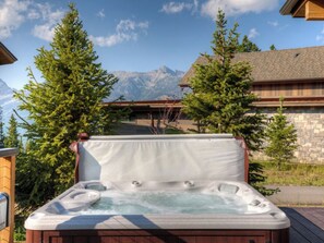 A hot tub with a view of mountains, surrounded by trees and a wooden deck.