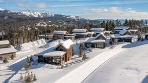 A snow-covered lodge with multiple wooden cabins, surrounded by snow-covered trees and mountains in the background. - Big Sky Vacation Rentals: Silvertip 22 Alpine Bend (big sky)