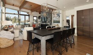 A modern kitchen with a large island, stone fireplace, and a dining area with a view of the outdoors.