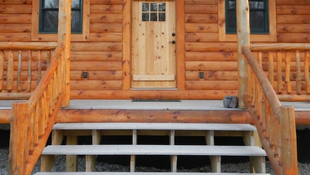 A wooden cabin with a front door, two windows, a staircase, and a light fixture above the door. - Jackson, NH Log Cabin near Storyland in White Mountains: 2Queen Bdrms+Sleep Loft (Jackson)
