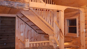 A wooden staircase with a patterned sofa in a cabin-style room. - Jackson, NH Log Cabin near Storyland in White Mountains: 2Queen Bdrms+Sleep Loft (Jackson)