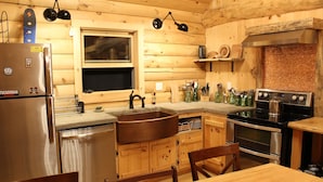 A wooden cabin-style kitchen with a stainless steel refrigerator, a sink, a stove, and wooden cabinets. - Jackson, NH Log Cabin near Storyland in White Mountains: 2Queen Bdrms+Sleep Loft (Jackson)