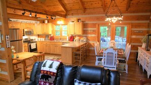 A log cabin interior with a kitchen, dining area, and a cozy seating area with a fireplace.