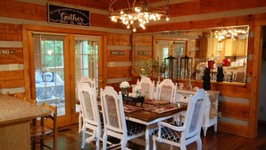 A wooden cabin interior with a dining area featuring white chairs and a wooden table.