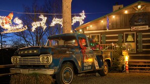 A vintage Ford truck parked in front of a building with Christmas decorations, including lights shaped like reindeer and a sleigh.
