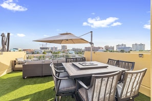 Une terrasse sur le toit, avec une table et des chaises, entourée d’une clôture blanche et offrant une vue sur le panorama urbain.