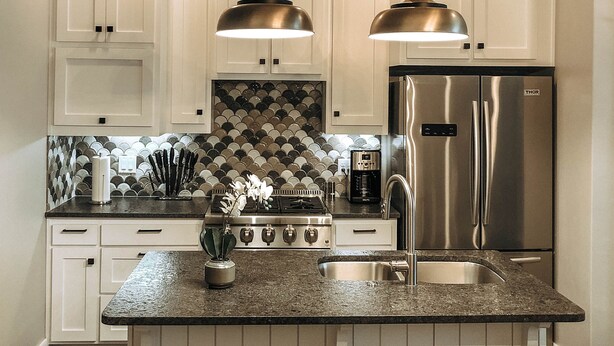 A modern kitchen with white cabinetry, a stainless steel refrigerator, a gas stove, and pendant lighting.