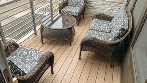 A balcony with wicker furniture, a glass-top table, and a stone wall backdrop.