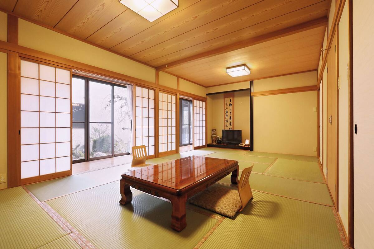 Ein traditioneller japanischer Raum mit Tatami-Böden, Schiebetüren, einem Holztisch und einem Fernseher.
