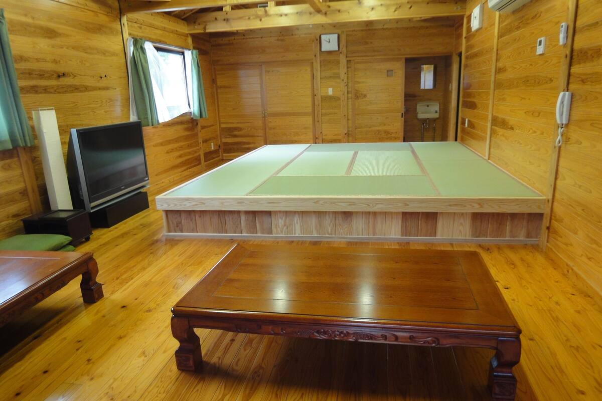 Ein Zimmer mit Holzboden, einem Tatami-Bodenbelag, einem Fernseher und einem Holztisch.
