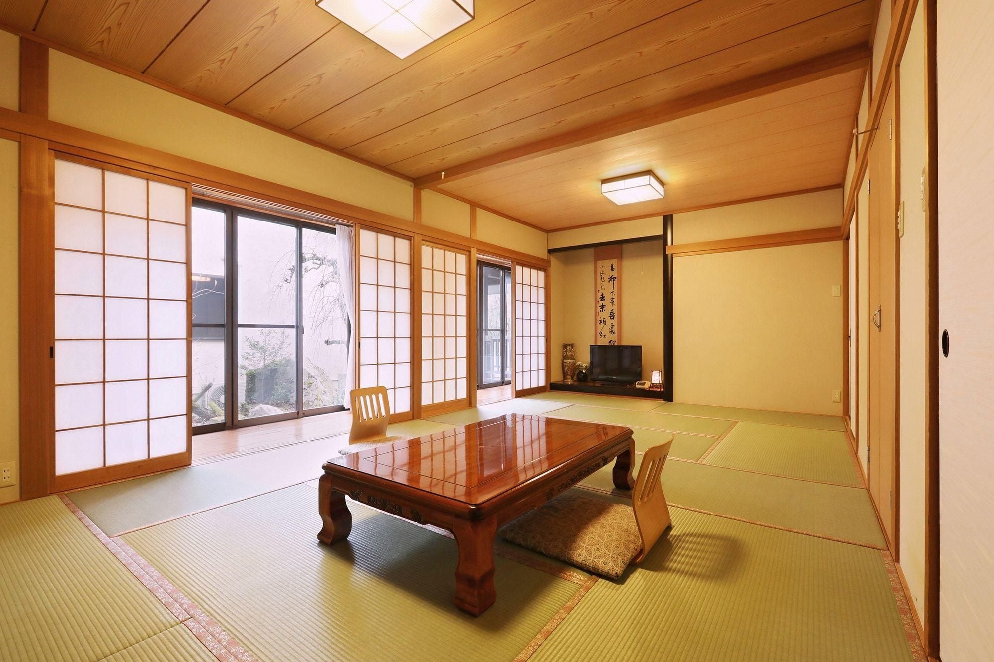 A traditional Japanese room with tatami flooring, a wooden table, sliding doors, and a television.