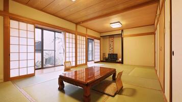 A traditional Japanese room with tatami flooring, a wooden table, sliding doors, and a television.