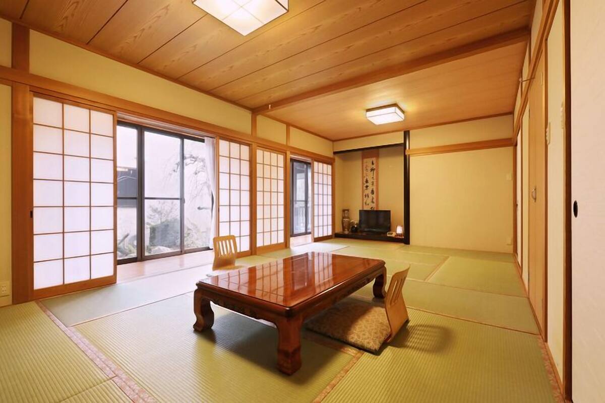 Ein traditioneller japanischer Raum mit Tatami-Bodenbelag, einem niedrigen Holztisch, Schiebetüren und einem Fernseher.