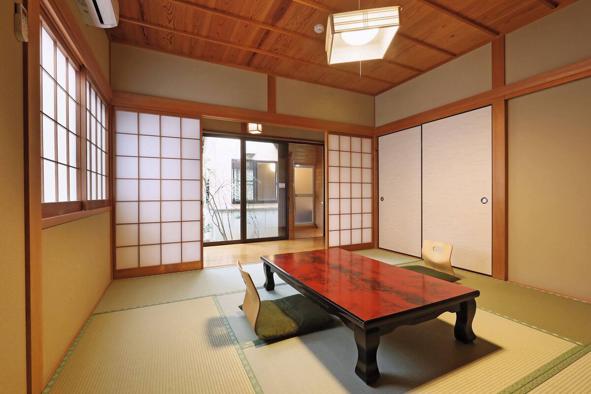 Ein traditioneller japanischer Raum mit Tatami-Boden, einem niedrigen Tisch, Schiebetüren und einem Deckenventilator.