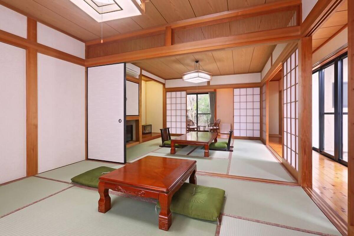 Ein traditioneller japanischer Raum mit Tatami-Böden, Holzmöbeln, Schiebetüren und Blick ins Freie.