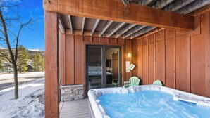 Une terrasse en bois avec un jacuzzi, une porte donnant sur une pièce et une chaise.