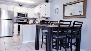 A modern kitchen with white cabinets, stainless steel appliances, and a dining area with a dark wooden table and chairs. - Great location, few steps from the beach!!! (Miramar Beach)