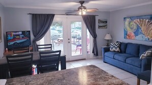 A living room with a blue sofa, a dining table with chairs, a ceiling fan, and a TV on a stand. - Great location, few steps from the beach!!! (Miramar Beach)