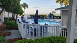 A pool area with a white fence, blue lounge chairs, and umbrellas. - Great location, few steps from the beach!!! (Miramar Beach)