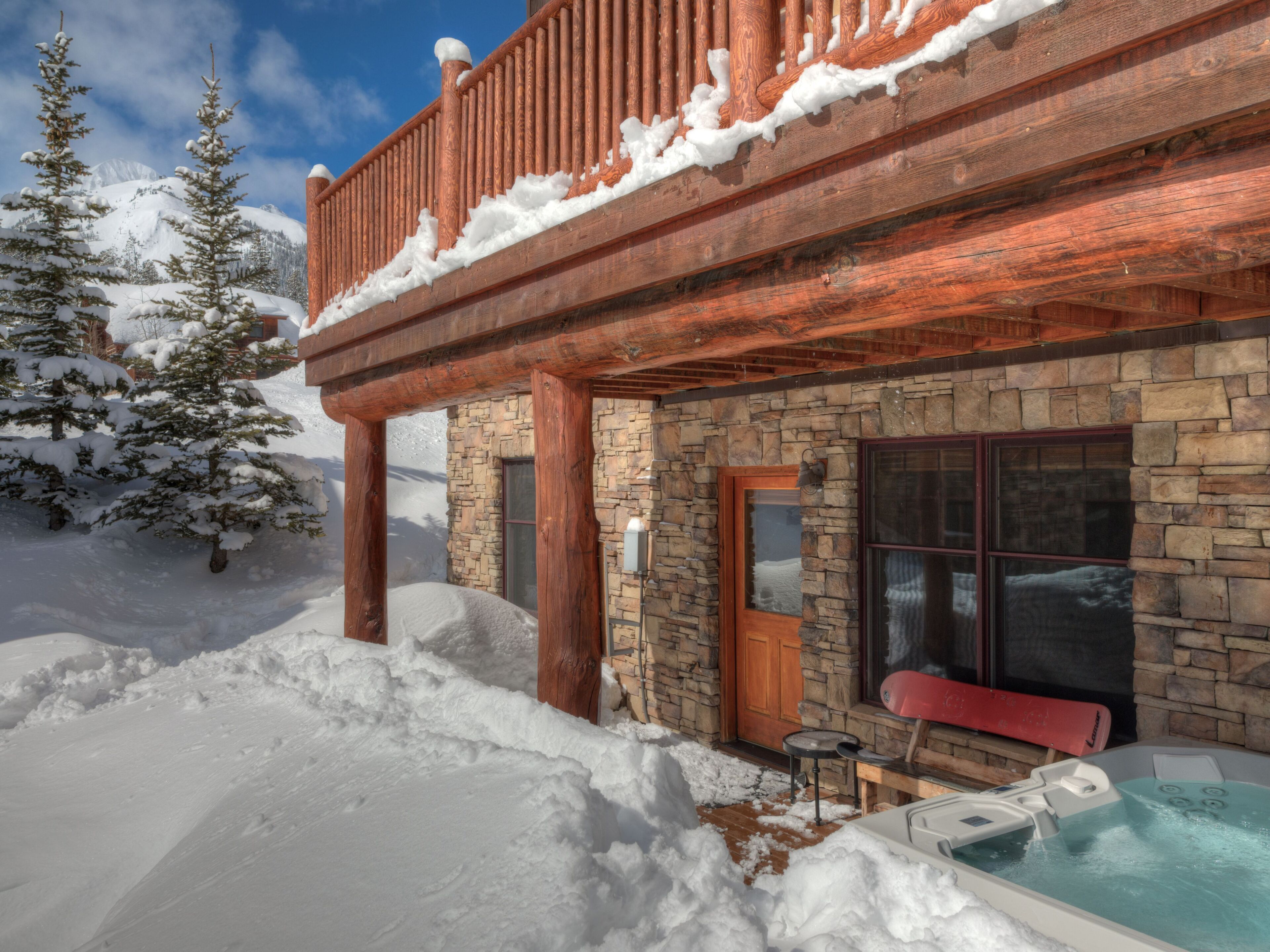 Une cabane en bois avec une façade en pierre, un jacuzzi et un environnement enneigé.