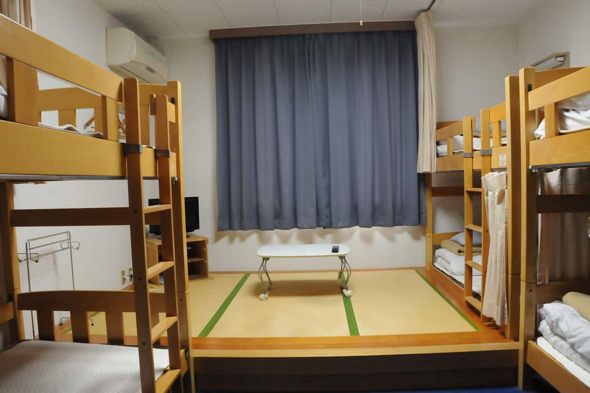 Une chambre de dortoir avec des lits superposés, une petite table et une fenêtre avec des rideaux.